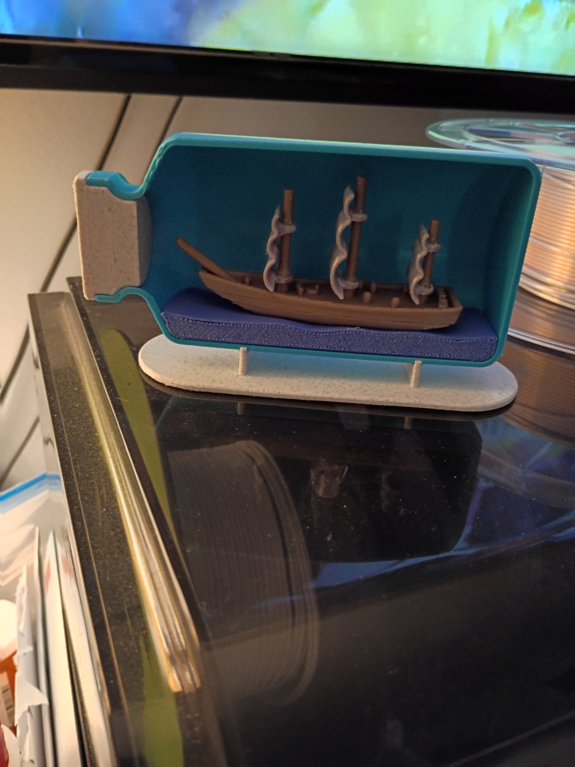 3D-printed ship in a bottle beside filament spools